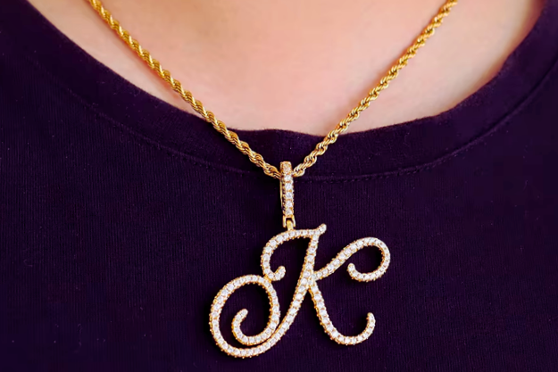 Gold necklace with a 'K' pendant on a person wearing a dark purple shirt.
