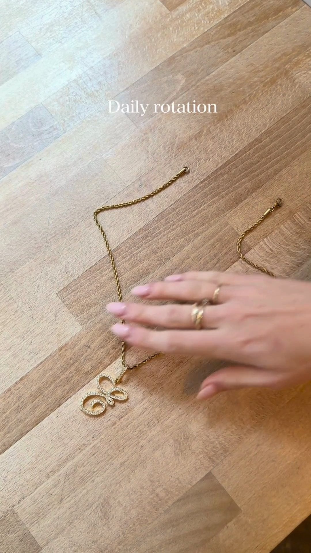 Gold necklace on a wooden surface with a hand and rings nearby, text 'Daily rotation' above.